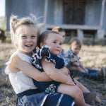 Baby in denim romper cuddled with sister
