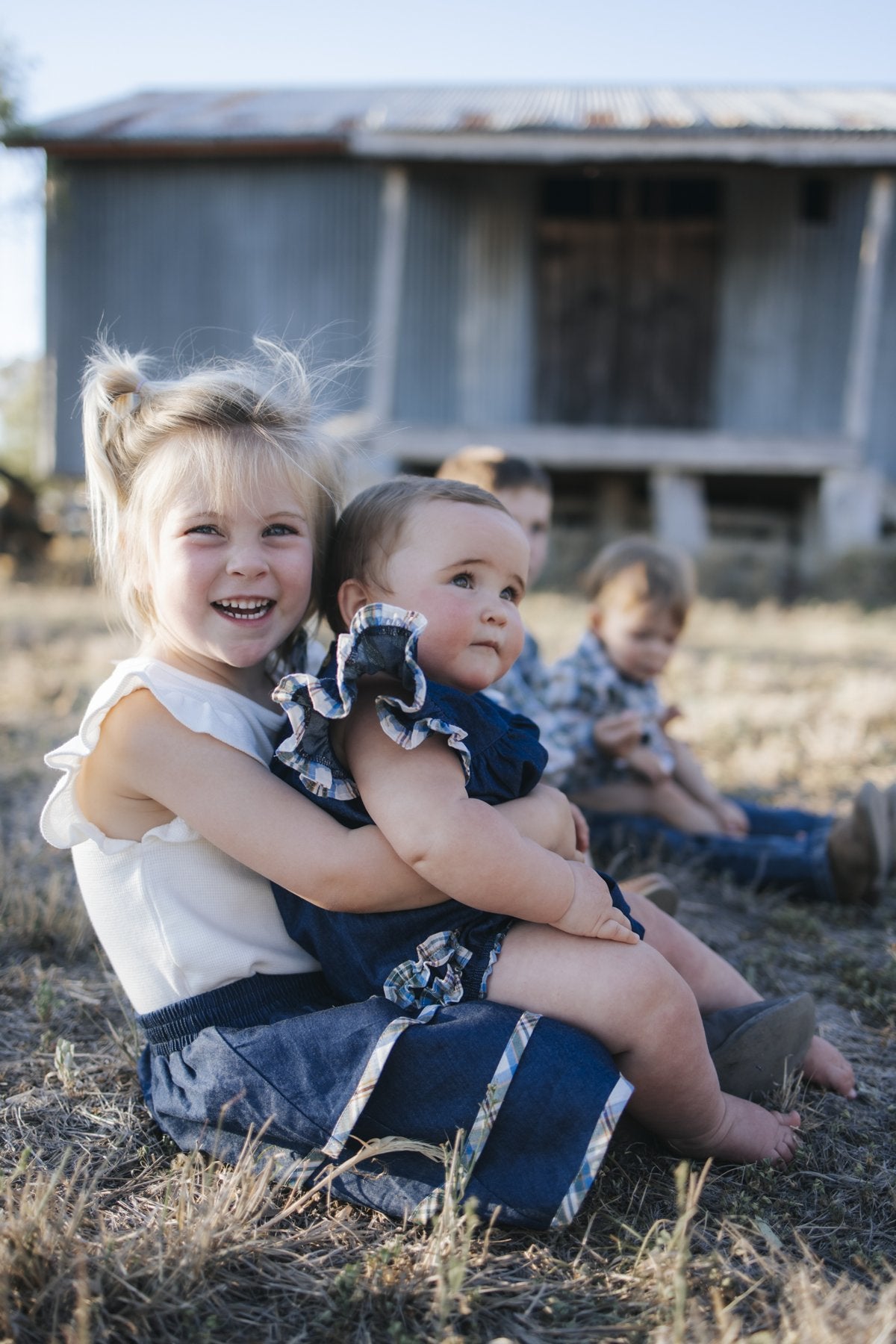 Baby in denim romper cuddled with sister