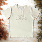 Beige t-shirt with 'Little Windmill Co' text on a wooden surface with decorative elements.
