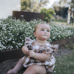 Baby in gingham flutter romper sitting in the garden