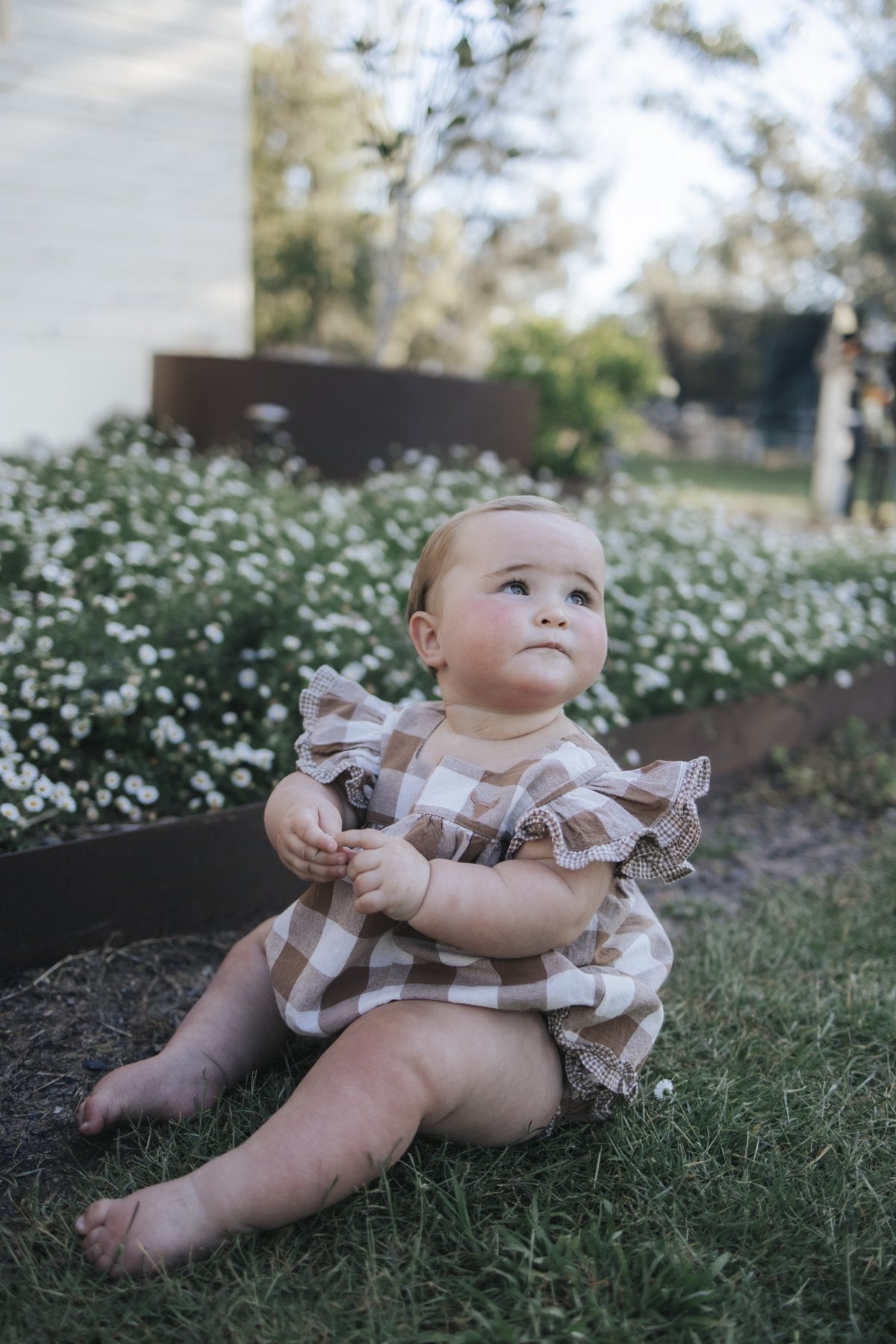 Baby in gingham flutter romper sitting in the garden