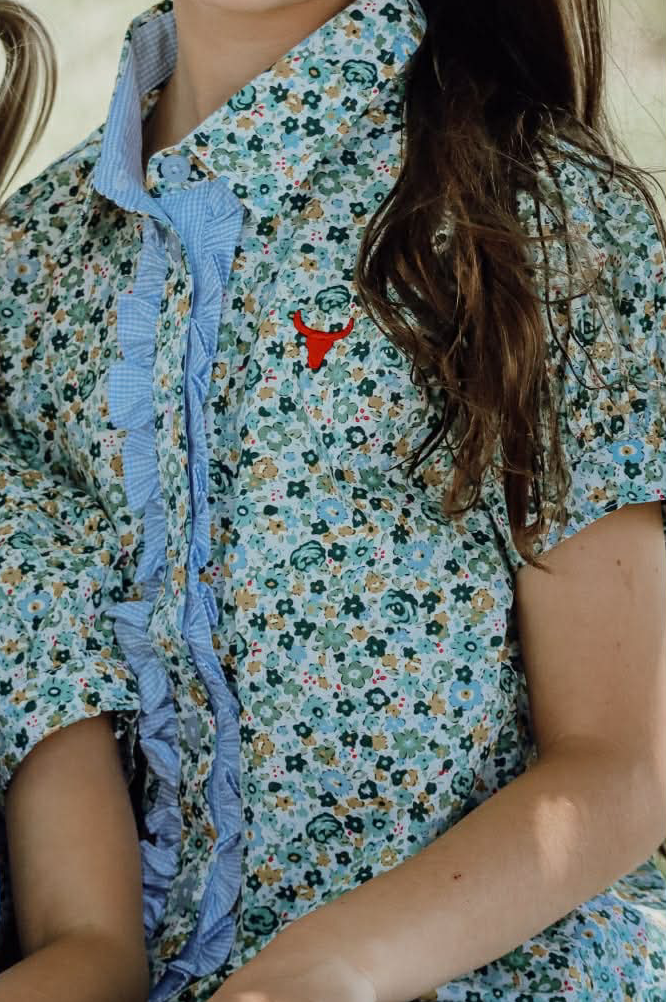 Three children in matching floral shirts sitting outdoors with a blurred natural background