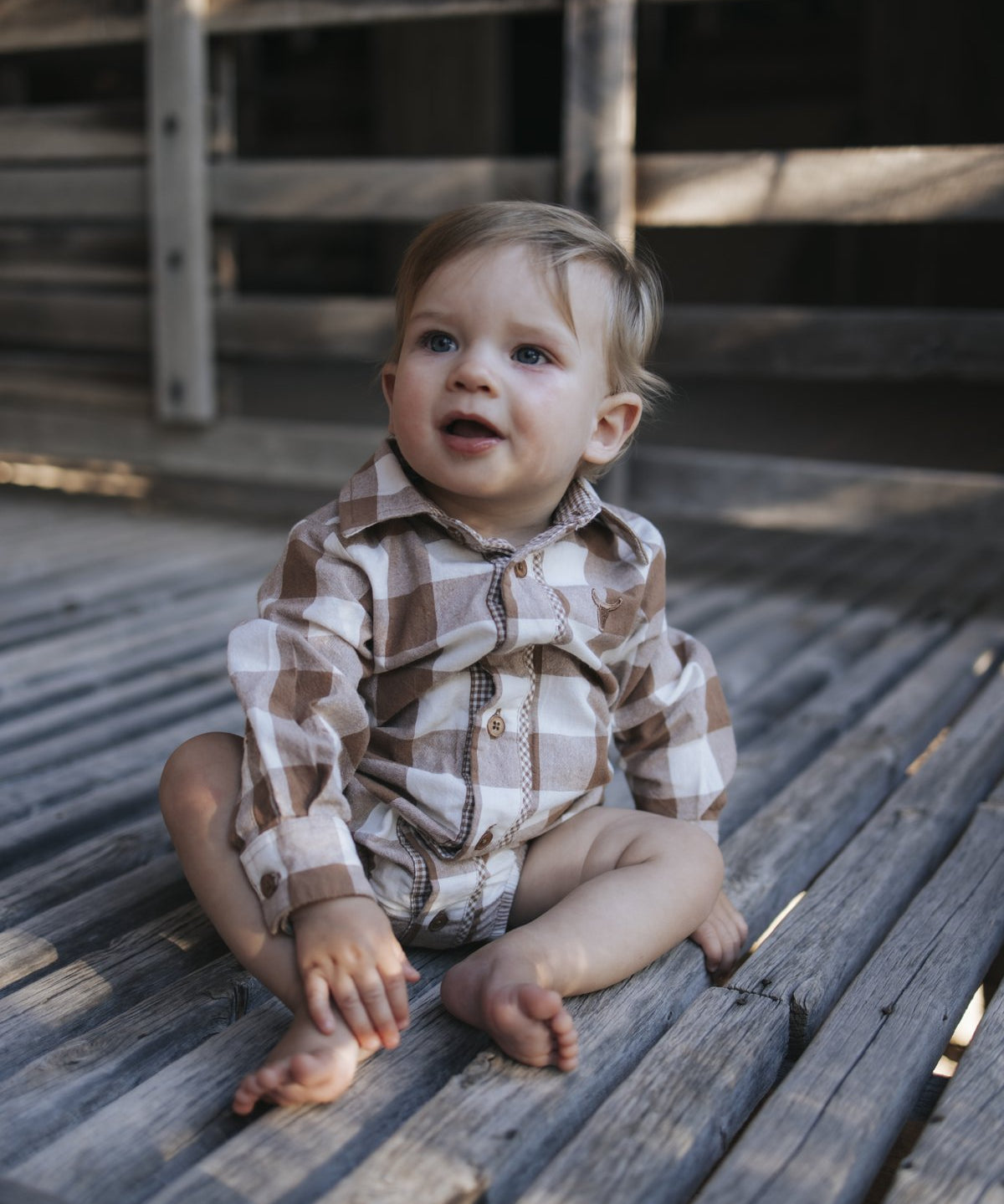 Baby boy in gingham bodysuit sitting on wooden boards