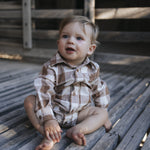 Baby boy in gingham bodysuit sitting on wooden boards