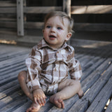 Baby boy in gingham bodysuit sitting on wooden boards