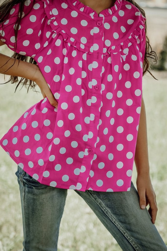 Person wearing a pink polka dot blouse with a blurred background
