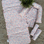 A floral baby travel seat pad set laid out on a concrete floor, featuring a large padded pad, a smaller matching pad, two rolled sections, and a small matching pillow, with a green plant placed on top.