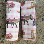 Two rolled fabric items with a pink and white gingham pattern and cowboy-themed illustrations, placed on a speckled stone surface.