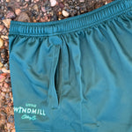 Teal shorts with a brand logo on a pebbly ground