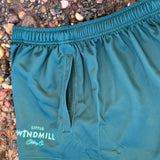 Teal shorts with a brand logo on a pebbly ground