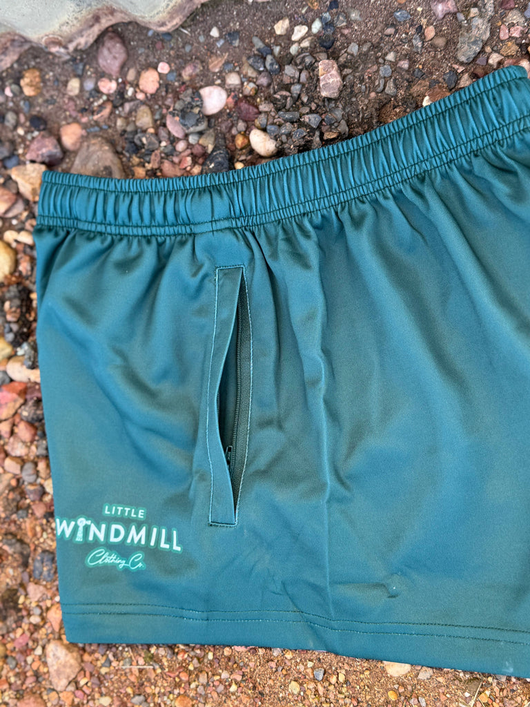 Teal shorts with a brand logo on a pebbly ground
