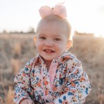 Child wearing a floral shirt with a pink bow in a field