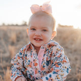 Child wearing a floral shirt with a pink bow in a field