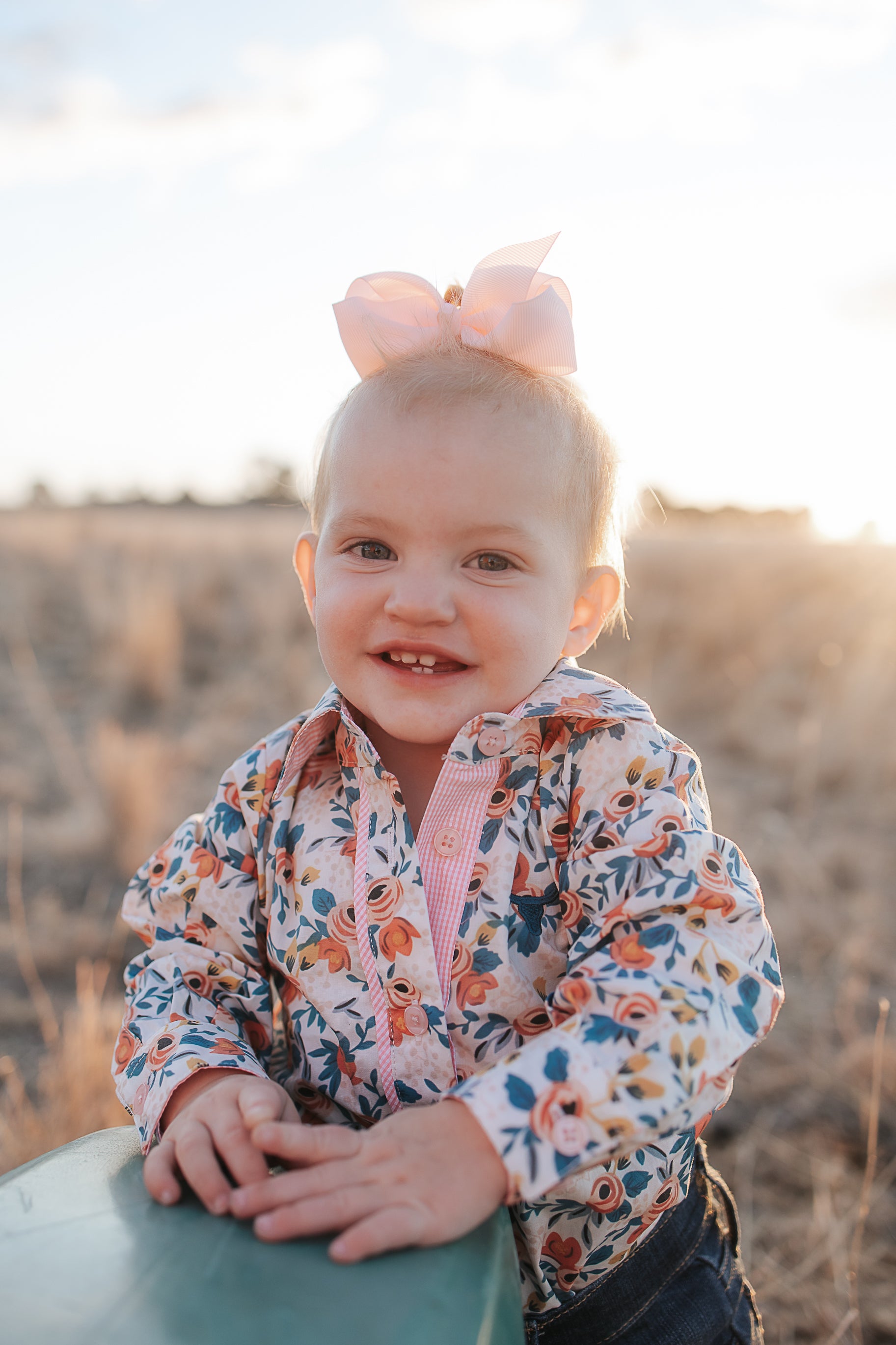 Child wearing a floral shirt with a pink bow in a field