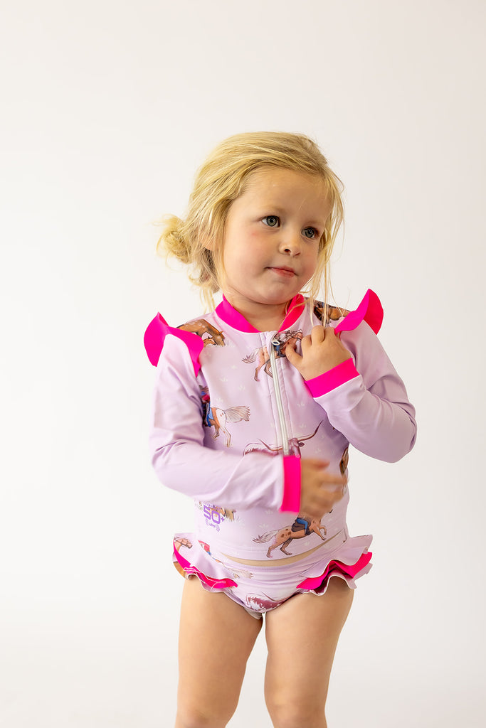 Child wearing a pink and purple swimsuit with cowgirl characters on a purple background