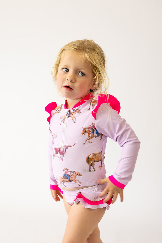 Child wearing a pink and white outfit swimmers with cowboy graphics on a white background