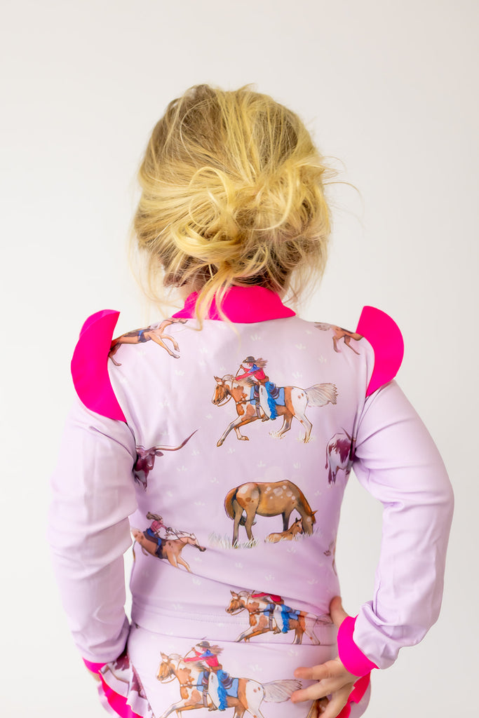 Person wearing a pink shirt with cowgirl and horse graphics on a purple background