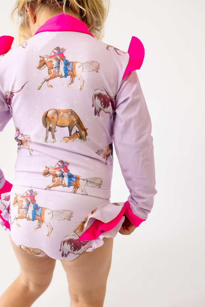 Child wearing a pink outfit with horse print on a white background