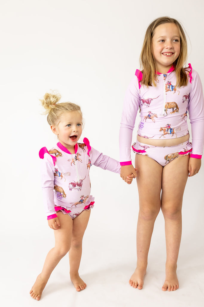 Two children wearing matching pink and white swimsuits with cartoon designs on a white background