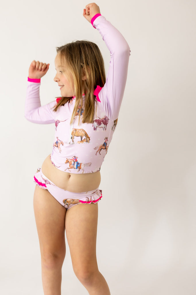 Child wearing a pink long-sleeve swimmers set with animal prints on a white background