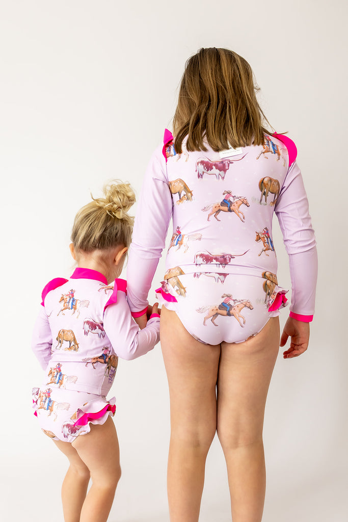 Two children wearing matching pink swimmers with animal prints on a white background