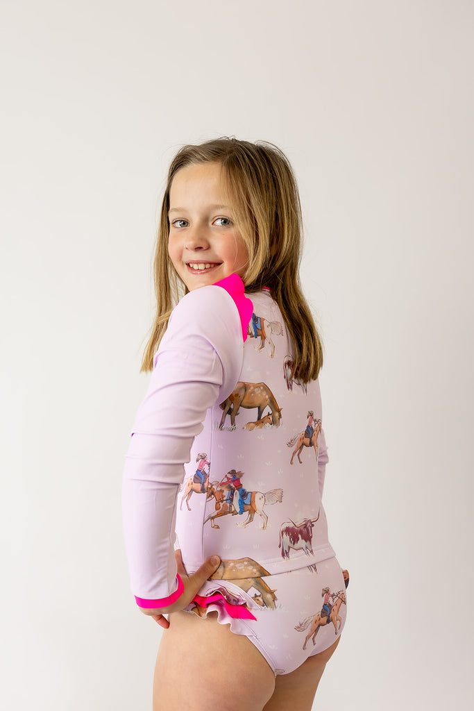 Child wearing a pink onesie with animal illustrations on a plain background