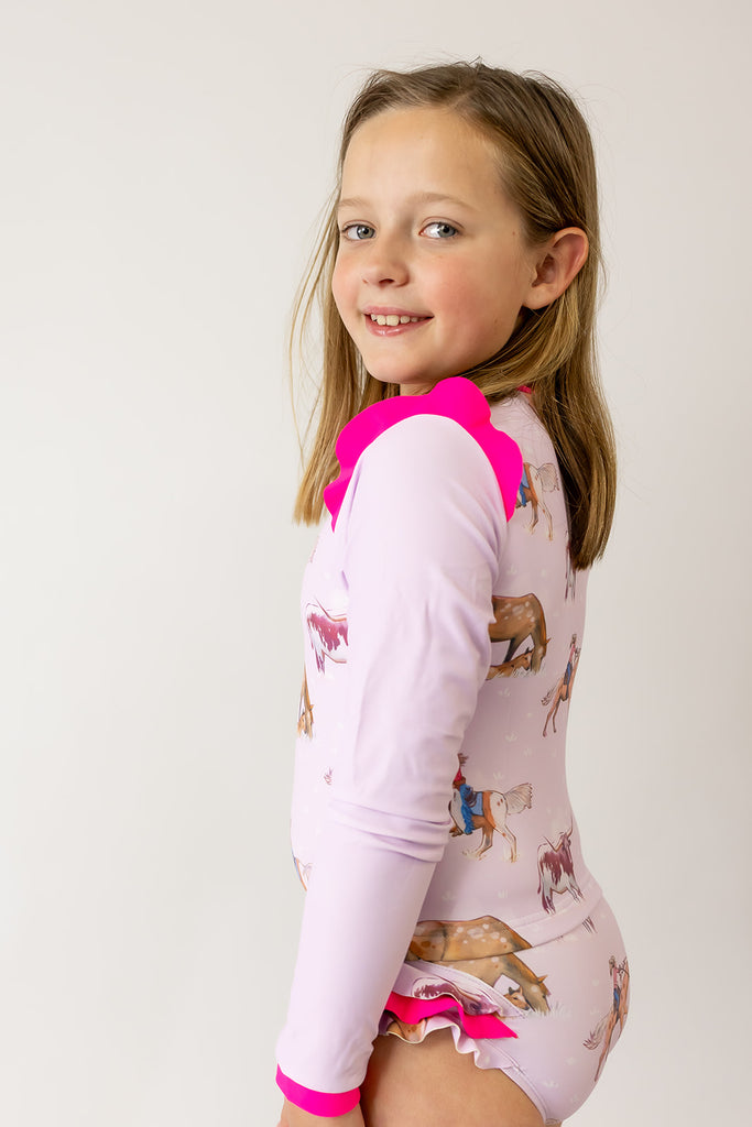 Young girl wearing a pink and white swimsuit with animal prints on a plain background