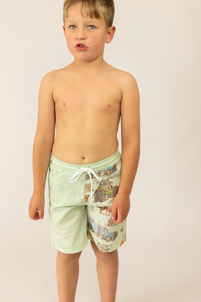 Young boy wearing light green swim shorts with a pattern on a plain background