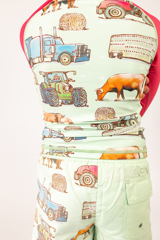 Boy wearing a rash shirt with farm animal and vehicle pattern