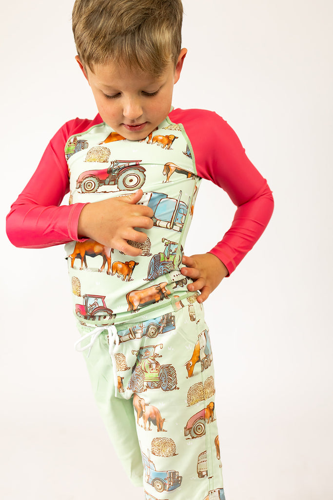 Child wearing a swimming rash shirt with farm animal and vehicle pattern on a green background