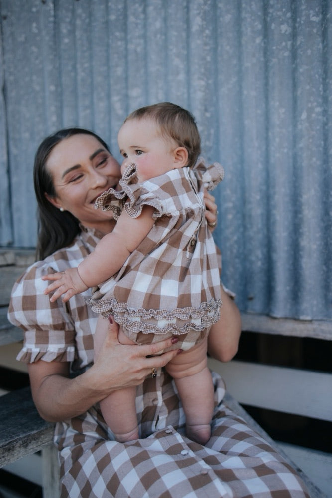 Mum holding baby girl in a brown gingham ruffle romper