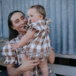 Mum holding baby girl in a brown gingham ruffle romper