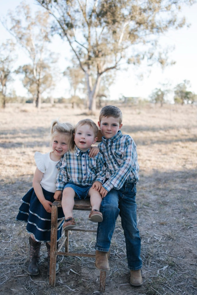 Three siblings in blue plaid shirts and a navy denim tiered skirt