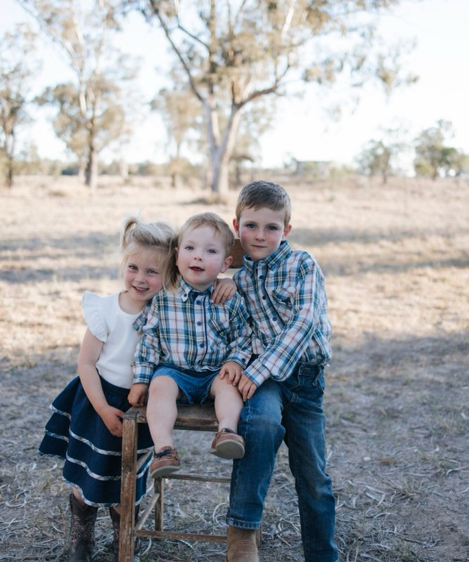 Three siblings in blue plaid shirts and a navy denim tiered skirt