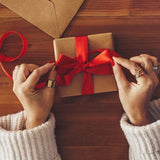 Hands tying a red ribbon around a gift box with gift wrap on a wooden table