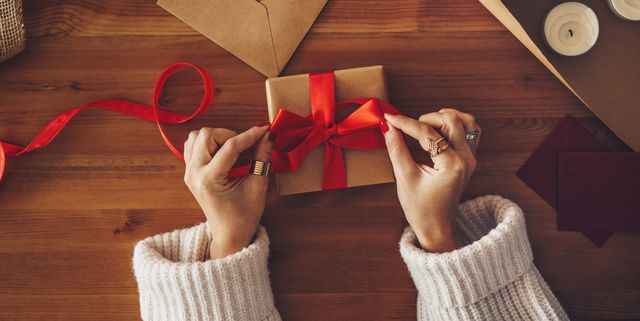 Hands tying a red ribbon around a gift box with gift wrap on a wooden table